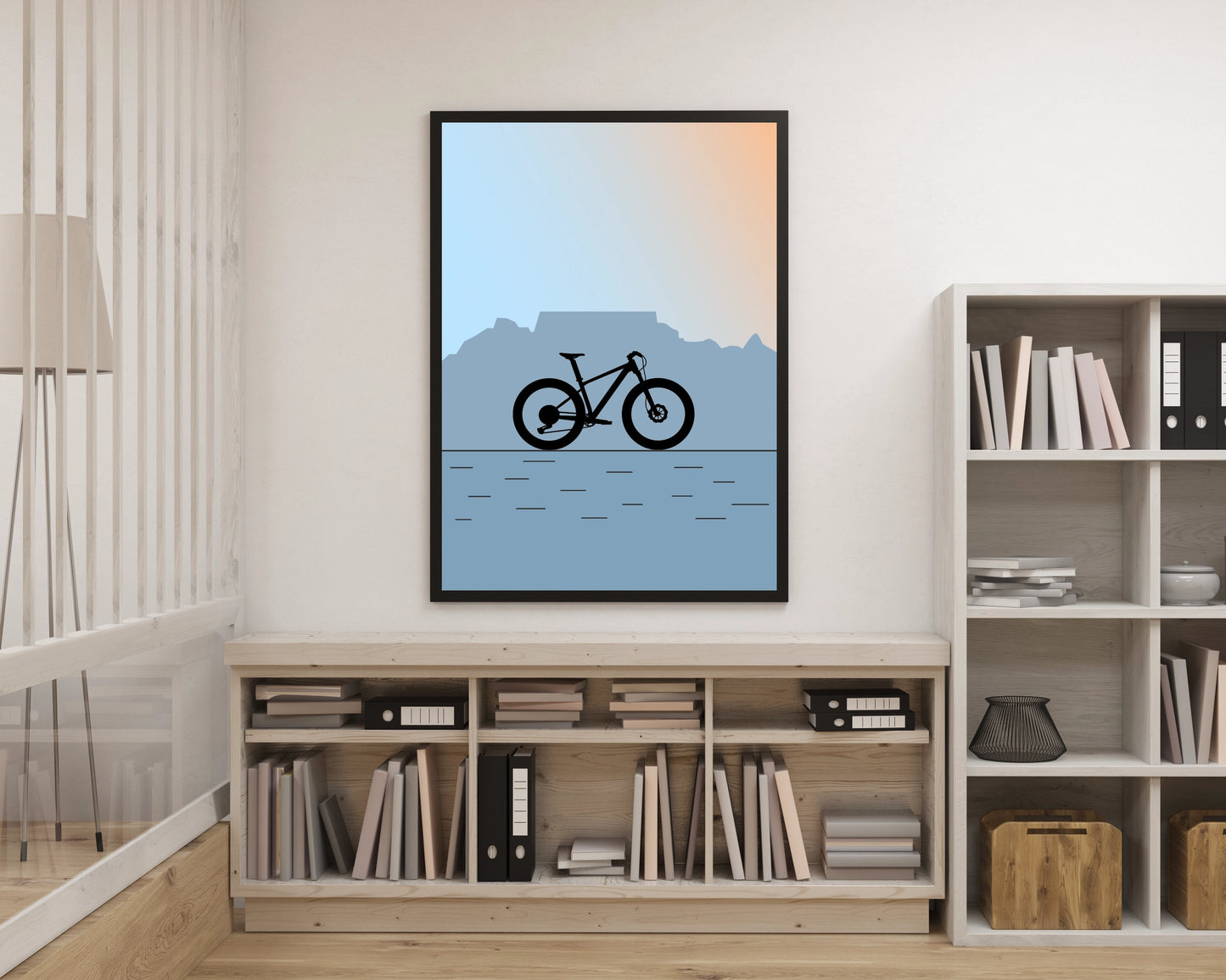 Framed artwork of a bicycle on a mountain landscape in a room with bookshelves.